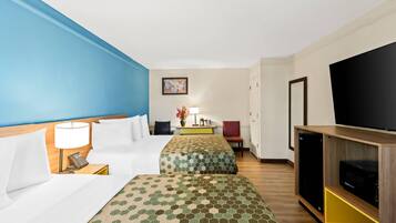 Habitación de hotel con dos camas, un televisor, un escritorio con lámpara y un cuadro en la pared.