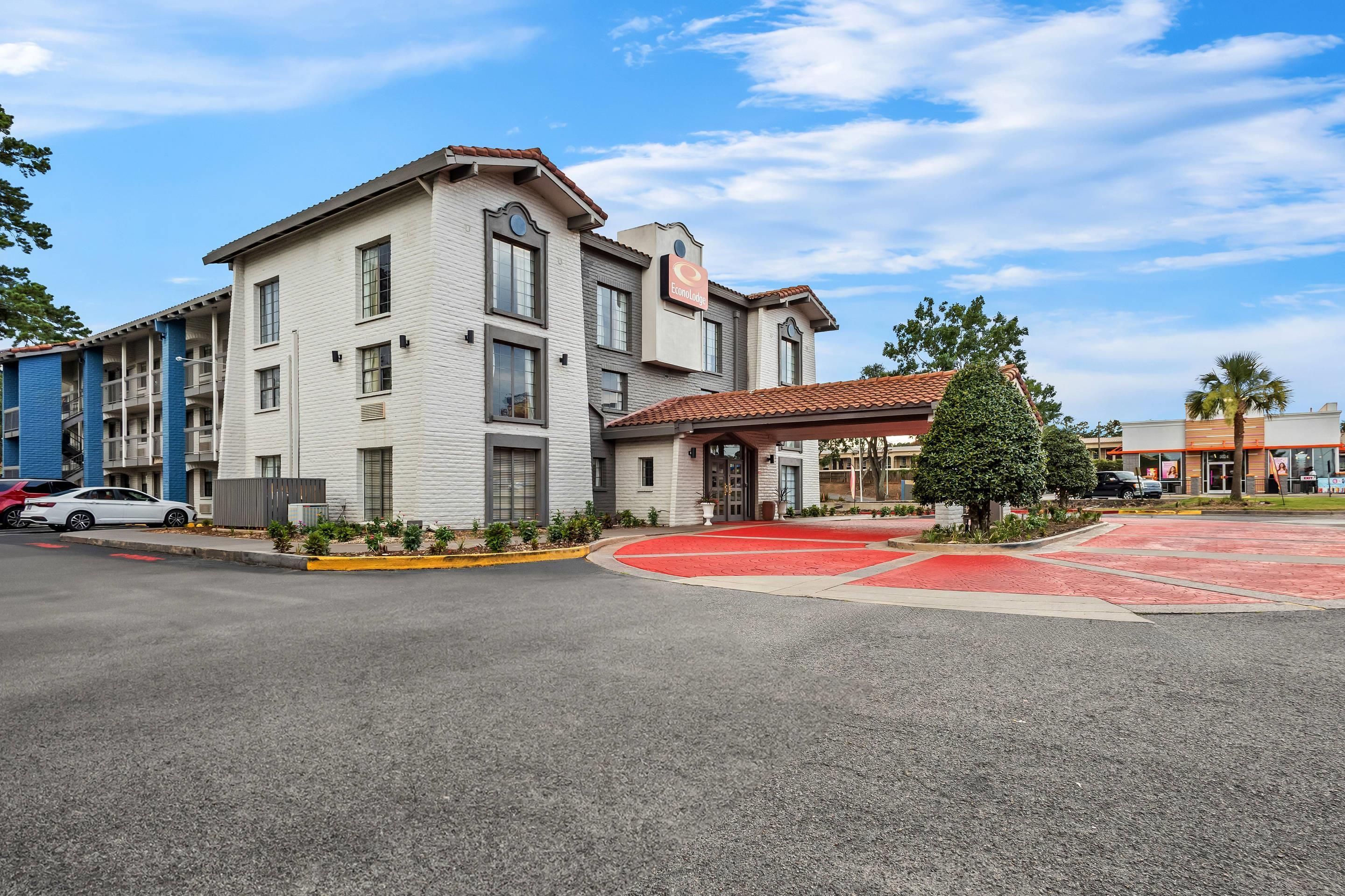 A multi-story hotel with a red carpet entrance, a covered outdoor area, and a clear blue sky.