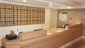 Een receptiebalie met een incheckgedeelte, een prikbord aan de muur en een deur met een bordje.