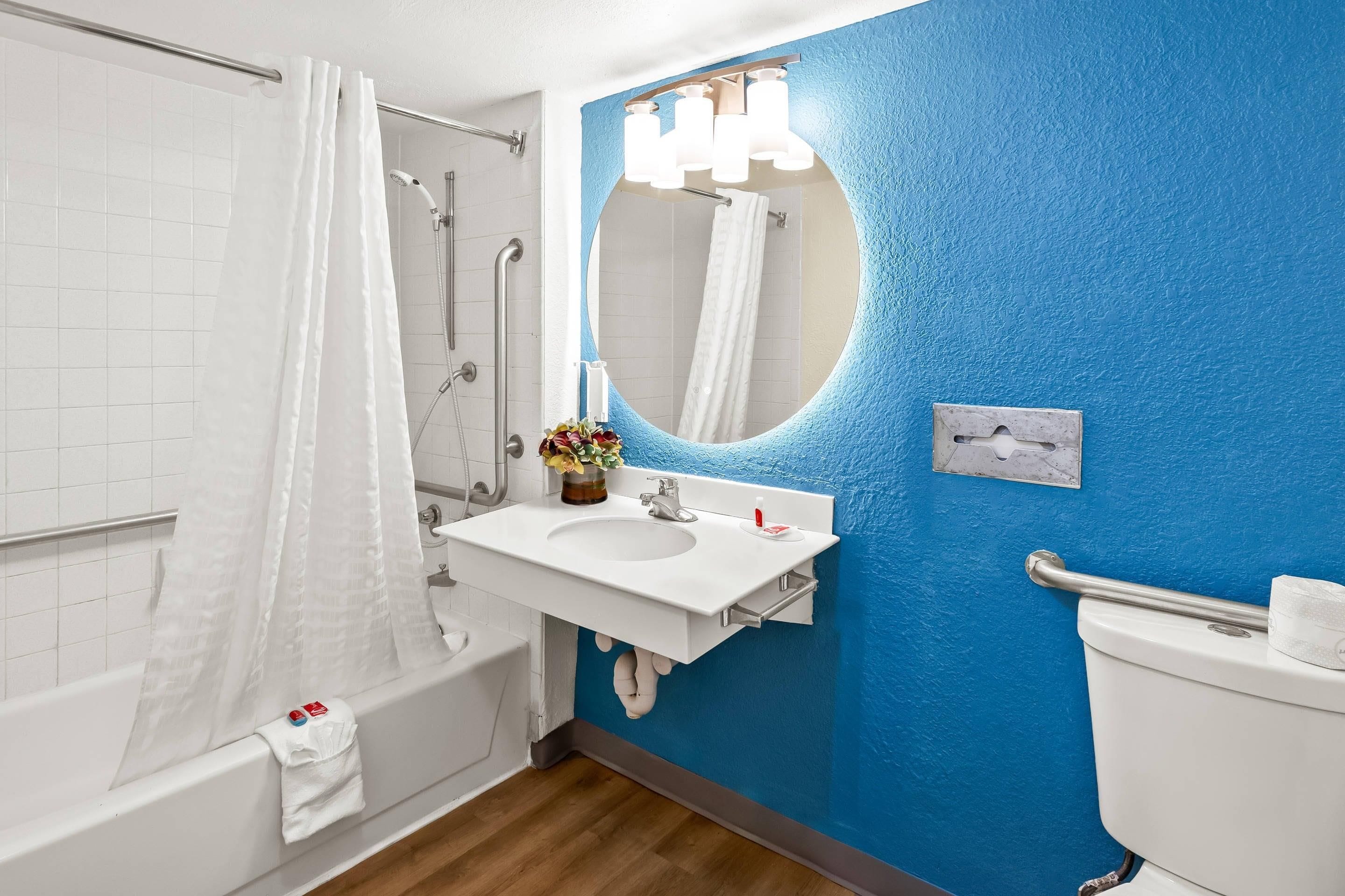 Un baño con una bañera blanca, un lavabo blanco y un espejo encima, y una pared azul.