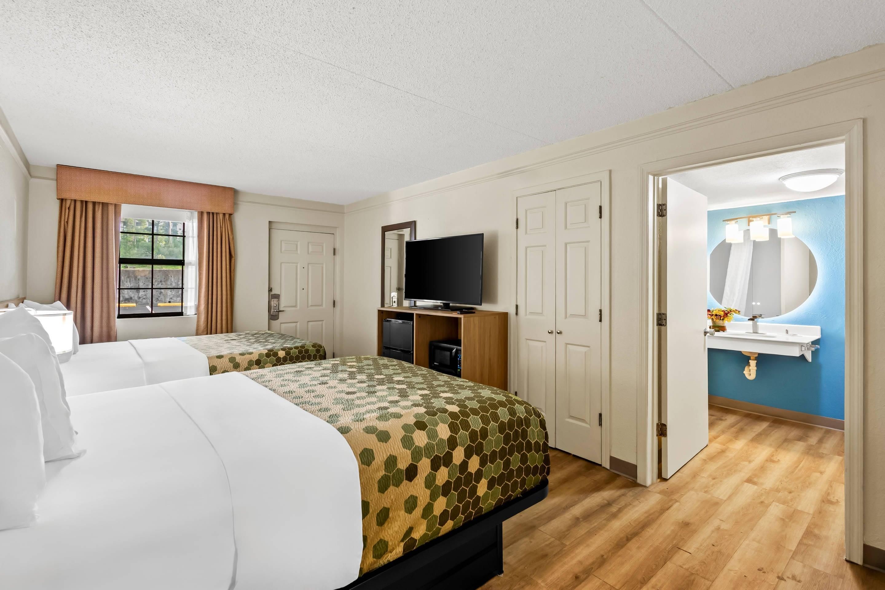 Une chambre d’hôtel avec deux lits, une télévision, une salle de bain avec un lavabo et un miroir, et une fenêtre avec des rideaux.