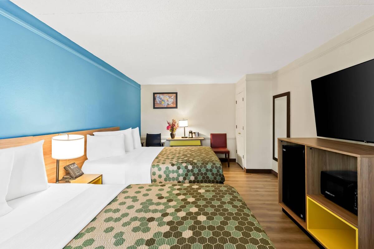 Habitación de hotel con dos camas, un televisor, un escritorio con lámpara y un cuadro en la pared.