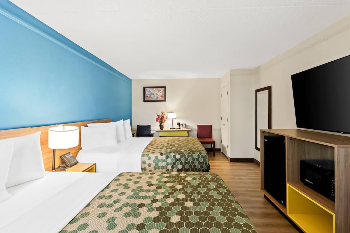 Une chambre d’hôtel avec deux lits, une télévision, un bureau avec une lampe et un tableau au mur.