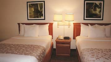 Habitación de hotel con dos camas, una mesita de noche con lámpara y dos cuadros en la pared.