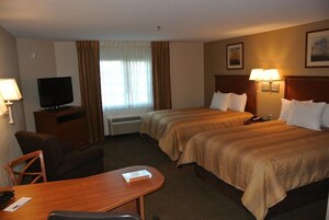Habitación de hotel con dos camas, un escritorio, una silla, un televisor y una ventana con cortinas.