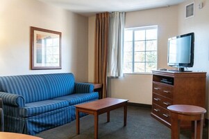 A living room with a blue sofa, a wooden coffee table, a TV on a wooden stand, and a window with curtains.
