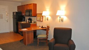 A compact kitchen with wooden cabinets, a microwave, and a coffee maker. There is a dining area with a wooden table and two chairs. Two wall-mounted lamps provide lighting. - Towneplace Suites by Marriott Birmingham South (Birmingham)