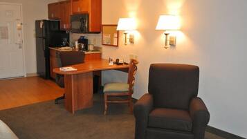 A compact kitchen with wooden cabinets, a microwave, and a coffee maker. There is a dining area with a wooden table and two chairs. Two wall-mounted lamps provide lighting.