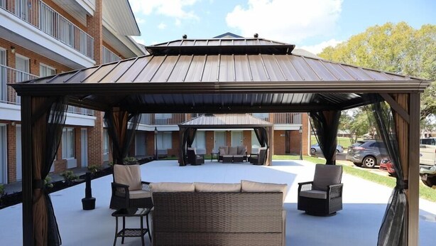 Un espace extérieur aménagé avec une pergola, des meubles en osier et une vue sur un bâtiment en arrière-plan.