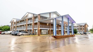 A multi-story hotel with a covered parking area and several cars parked in front. - Days Inn & Suites by Wyndham Bossier City (Bossier City)