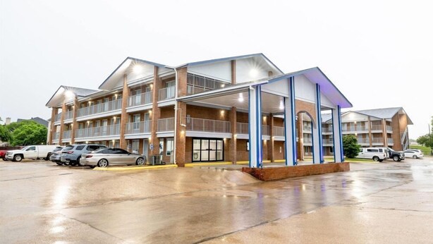 A multi-story hotel with a covered parking area and several cars parked in front. - Days Inn & Suites by Wyndham Bossier City (Bossier City)