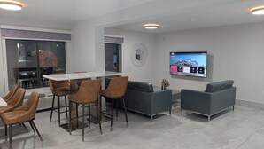 A modern living room with a dining area, grey sofas, and a TV mounted on the wall. - Days Inn & Suites by Wyndham Bossier City (Bossier City)
