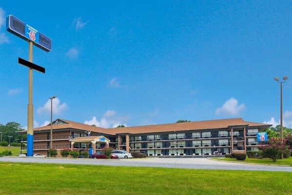 A multi-story hotel with a parking lot and a sign indicating it is on route 6. - Motel6 Macon, GA (Macon)