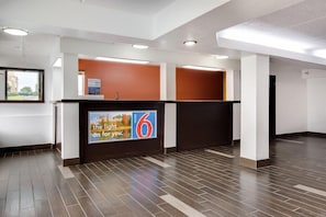 A hotel reception area with a modern design, featuring a reception desk, a large sign advertising a motel, and a view of the outside through a window. - Motel6 Macon, GA (Macon)