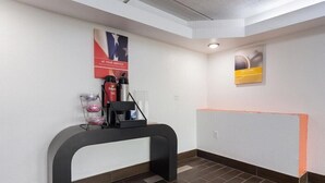 Ein Empfangsbereich mit einem schwarzen Empfangstresen, einer Kaffeemaschine und einem Poster an der Wand.