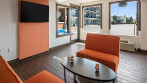 Ein modernes Hotelzimmer mit großem Fenster, einem wandmontierten Flachbildfernseher, einem orangefarbenen Sofa und einem kleinen runden Tisch.