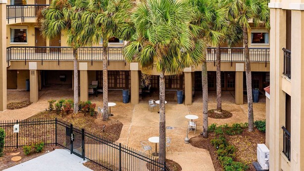 A multi-level courtyard with palm trees, outdoor seating, and a black metal fence. - Comfort Suites Baton Rouge South I-10 (Baton Rouge)