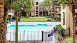 A pool area with a fence, palm trees, and a building with balconies in the background. - Comfort Suites Baton Rouge South I-10 (Baton Rouge)