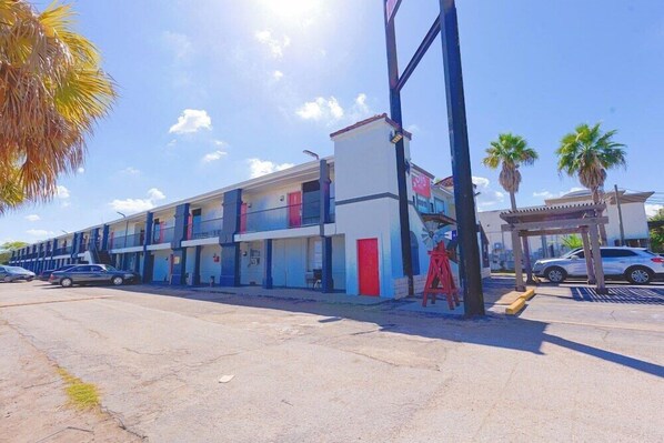 Un motel à plusieurs étages doté de balcons, d’un parking et de palmiers.