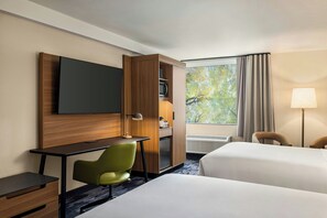 Een hotelkamer met een bureau, een groene stoel, een televisie, een kledingkast, een bed, een raam met gordijnen, en een lamp.