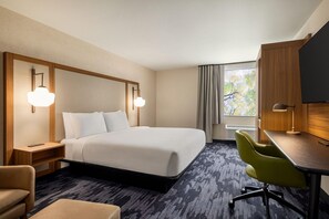 Una camera d'albergo con un letto grande, una scrivania con una sedia, una televisione e una finestra con tende.