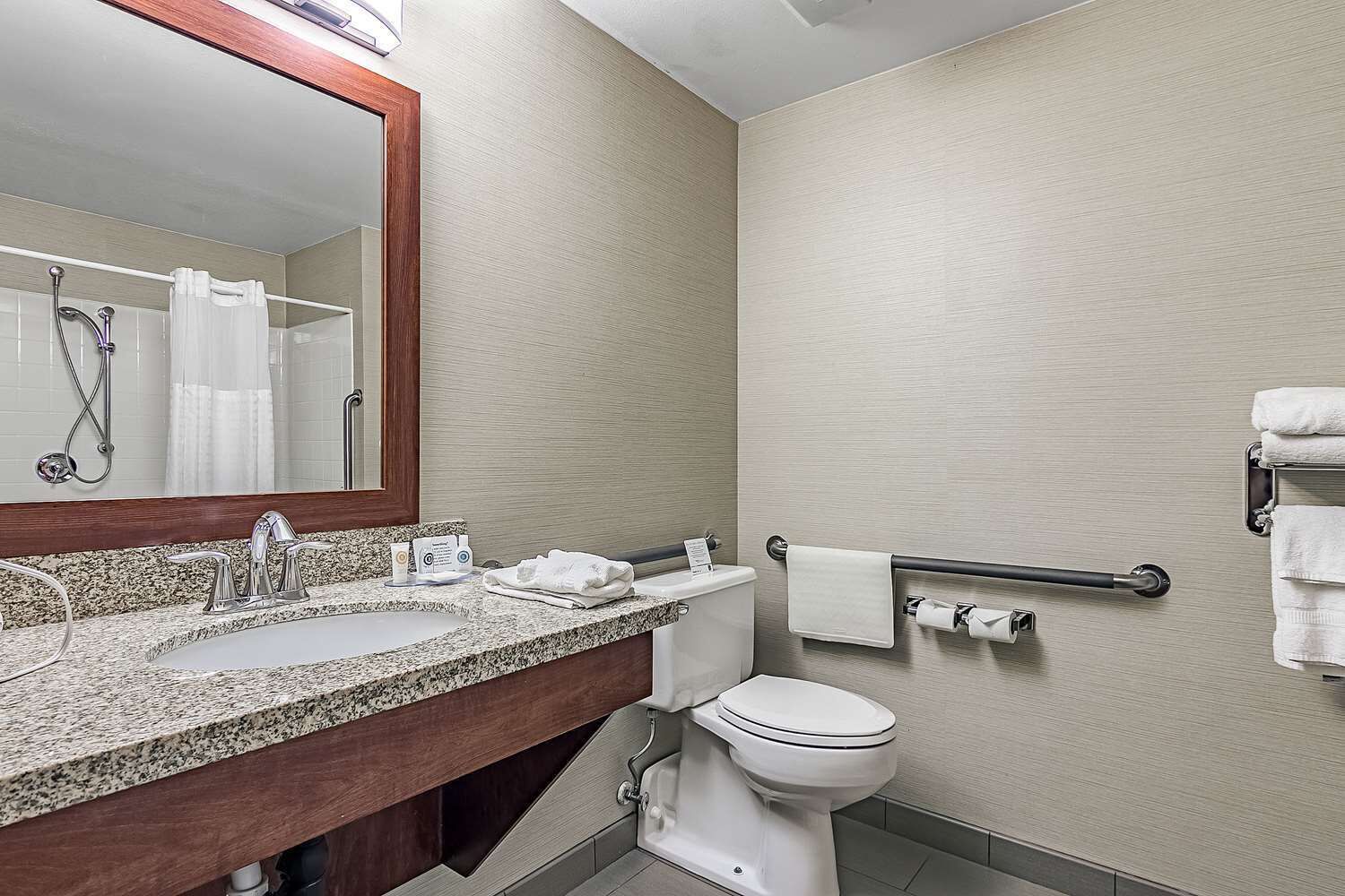 A bathroom with a granite countertop sink, a toilet, a shower with a curtain, and a towel rack.