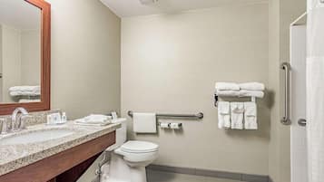 A modern bathroom with a granite countertop sink, a white toilet, a towel rack with towels, a handrail, and a shower area.