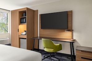 A hotel room with a bed, a desk with a chair, a flat-screen TV, a lamp, and a built-in shelf with a microwave and a coffee maker. - Hotel Monona (Madison)