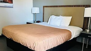 A hotel room with a large bed, a wooden headboard, a nightstand with a lamp, and a herringbone-patterned floor. - Blisspoint Inn Northwest Indianapolis (Indianapolis)