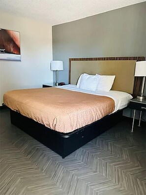 Habitación de hotel con una cama grande, cabecera de madera, mesita de noche con lámpara y suelo con estampado tipo espiga.