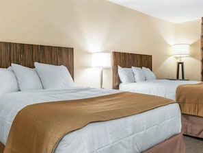 Habitación de hotel con dos camas, cada una con ropa blanca y una manta marrón. Hay dos lámparas de noche y un cabecero de madera.