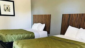 A hotel room with two single beds, each with a green bedspread and white pillows. The room has a herringbone-patterned floor and a wooden headboard. - Blisspoint Inn Northwest Indianapolis (Indianapolis)