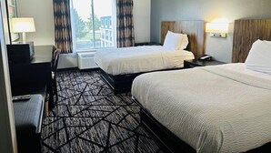 A hotel room with two beds, a desk, a chair, a lamp, and a view of the outdoors. - Blisspoint Inn Northwest Indianapolis (Indianapolis)