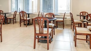A dining area with multiple tables and chairs, large windows with blinds, and a flat-screen TV mounted on the wall. - Fairbridge Inn Express Indianapolis Northwest (Indianapolis)