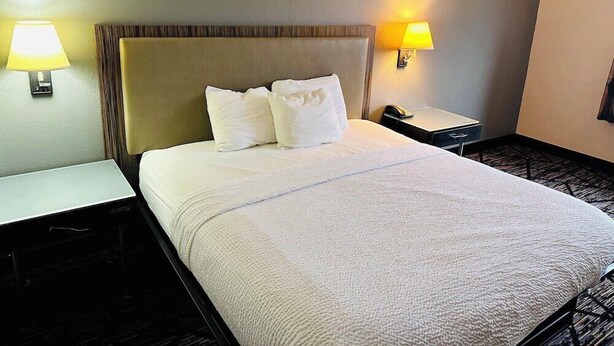 A hotel room with a bed, two bedside tables, and two wall-mounted lamps. - Blisspoint Inn Northwest Indianapolis (Indianapolis)
