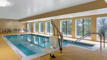 An indoor swimming pool with a lifeguard chair, a pool ladder, and a windowed wall.