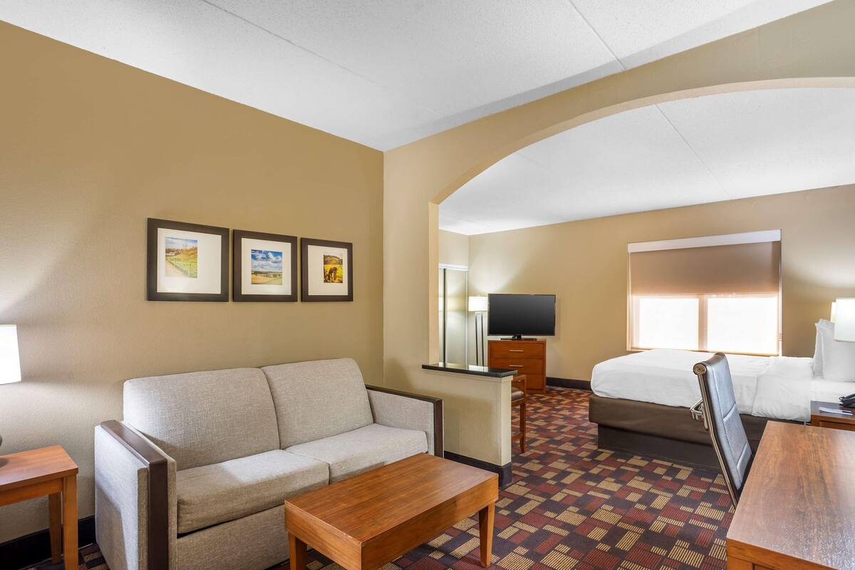 A hotel room with a sofa, a wooden table, a bed, a TV, and framed pictures on the wall.