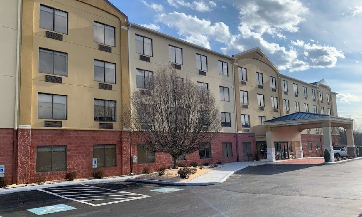 A multi-story hotel with a parking lot, a covered entrance, and a tree in front.