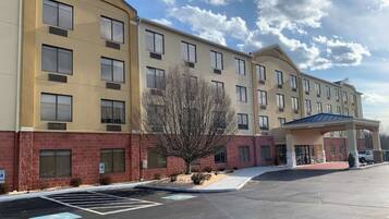 A multi-story hotel with a parking lot, a covered entrance, and a tree in front.