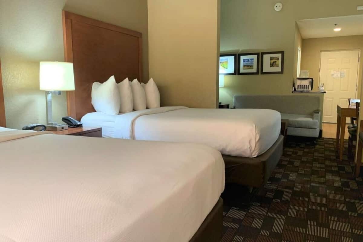 A hotel room with two beds, a desk, a chair, and a lamp.