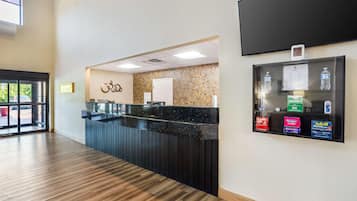 A reception area with a wooden floor, a reception desk, a wall-mounted TV, and a display case with bottled water and allergy medication.