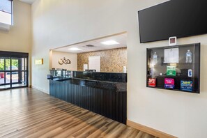 A reception area with a wooden floor, a reception desk, a wall-mounted TV, and a display case with bottled water and allergy medication. - Best Western Grantville/hershey (Grantville)