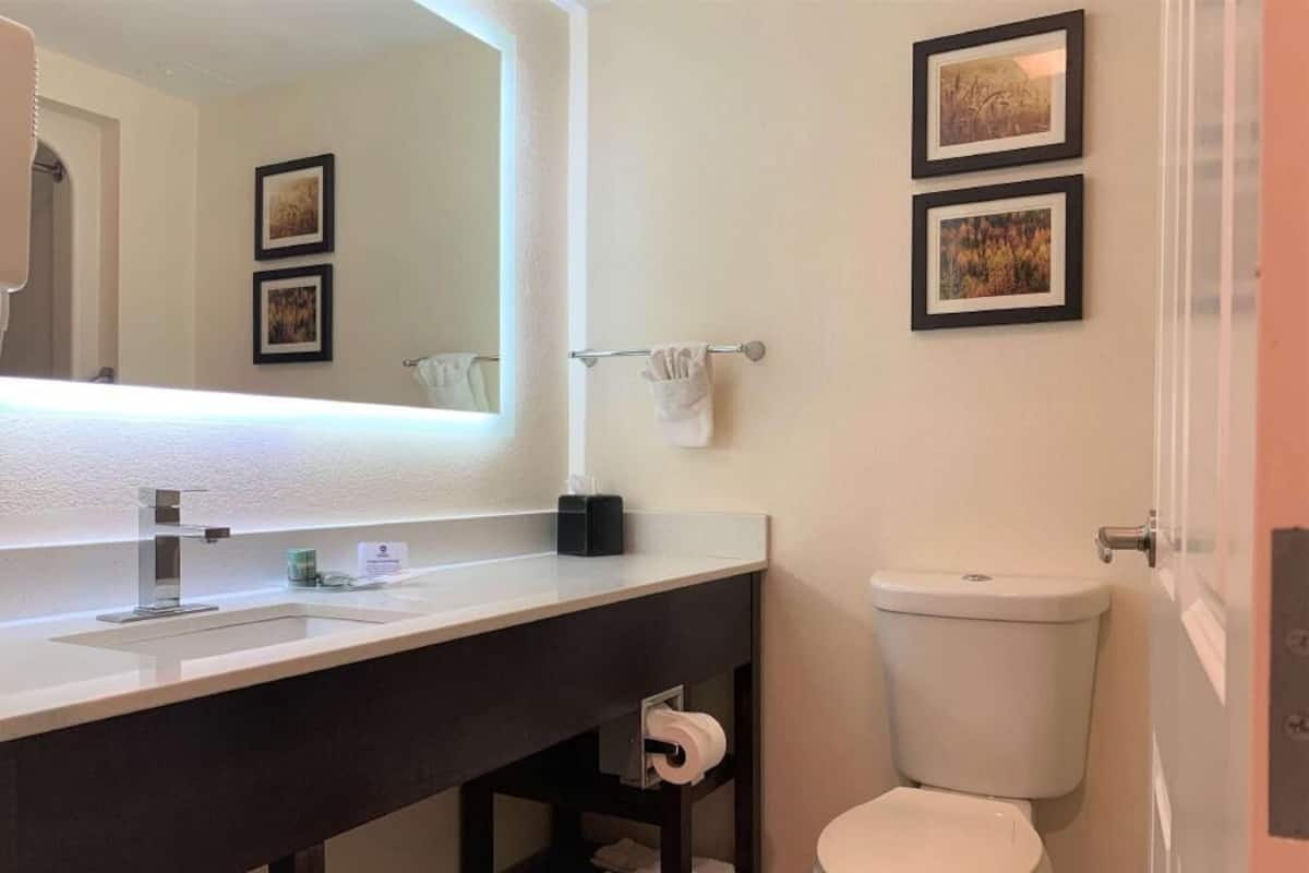 A bathroom with a white sink, dark vanity, toilet, and two framed pictures on the wall.