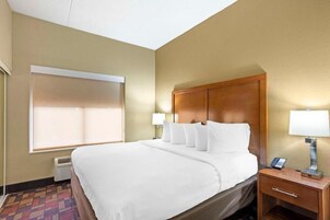 Una habitación de hotel con una cama grande, lámparas de noche, un teléfono y una ventana con persianas.