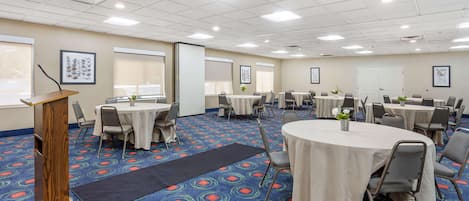 Une salle de conférence équipée d’un pupitre, de tables rondes, de chaises et d’un tapis à motifs.