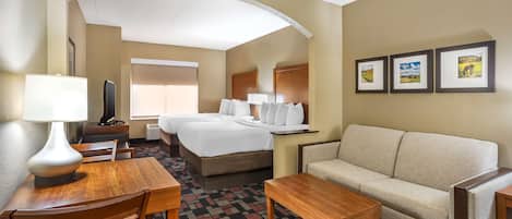 A hotel room with a bed, sofa, dining table, chairs, and a TV.