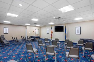 A conference room with a blue carpet, rows of chairs, a table, flags, and a TV screen.