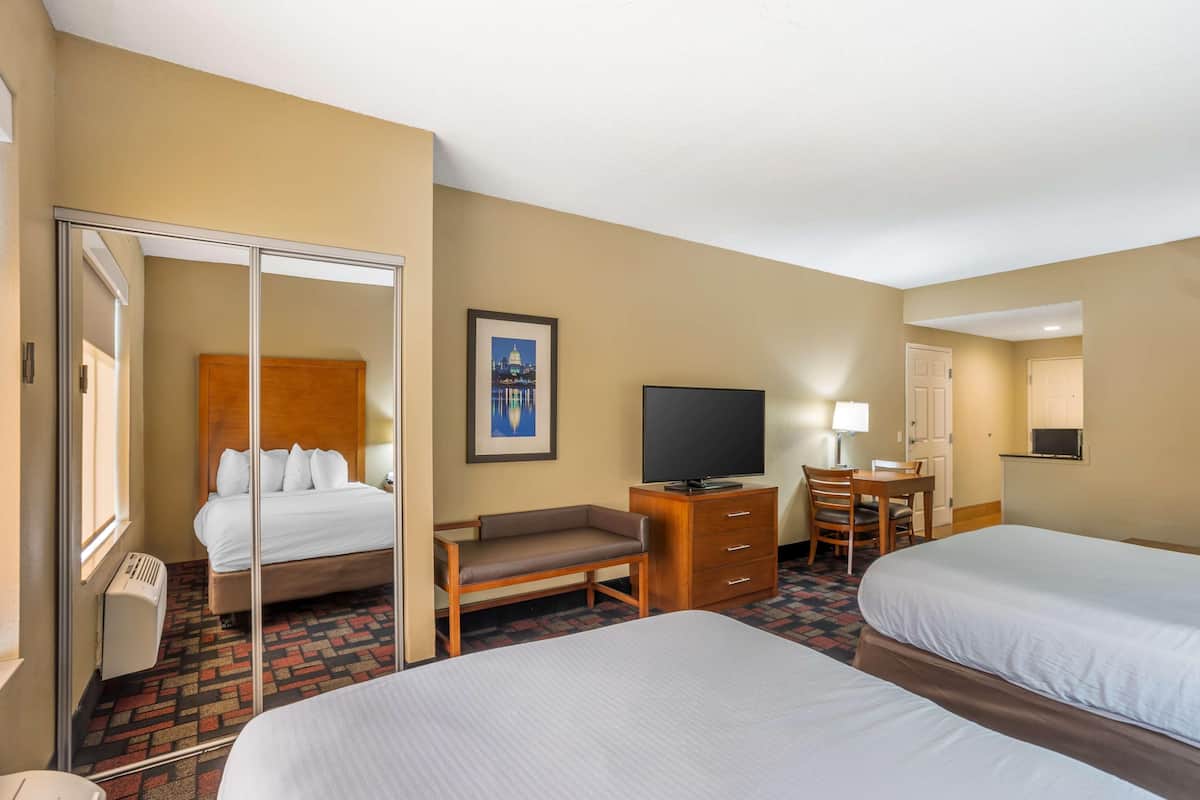 A hotel room with two beds, a desk, a chair, a television, and a framed picture on the wall.