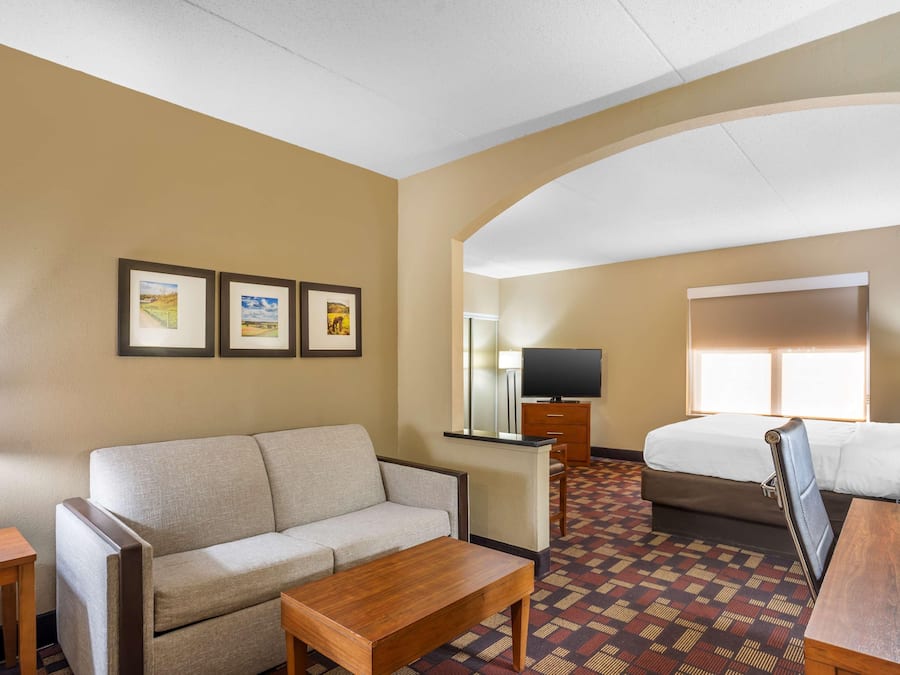 Quarto de hotel com sofá, mesa de madeira, cama, televisão e quadros nas paredes.