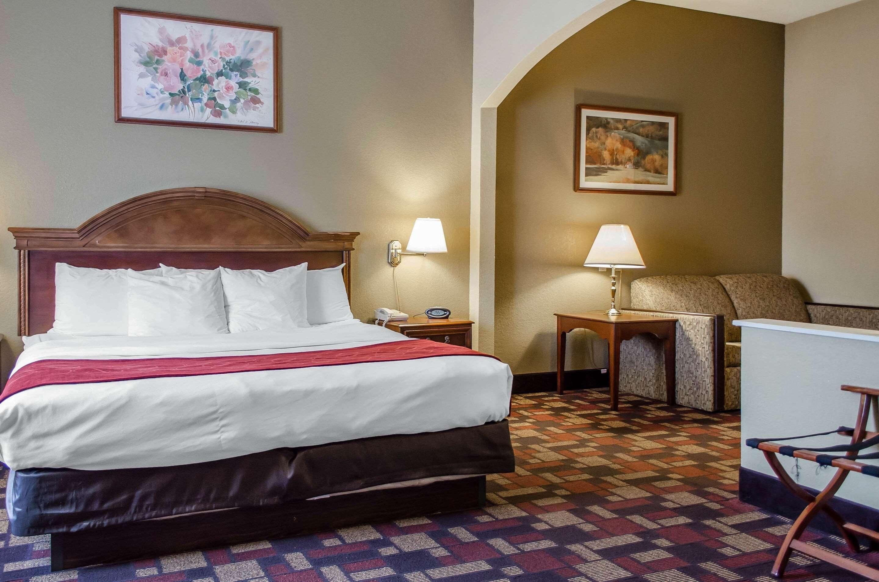 Habitación de hotel con una cama grande, dos lámparas de noche, una silla, una mesita y un cuadro en la pared.